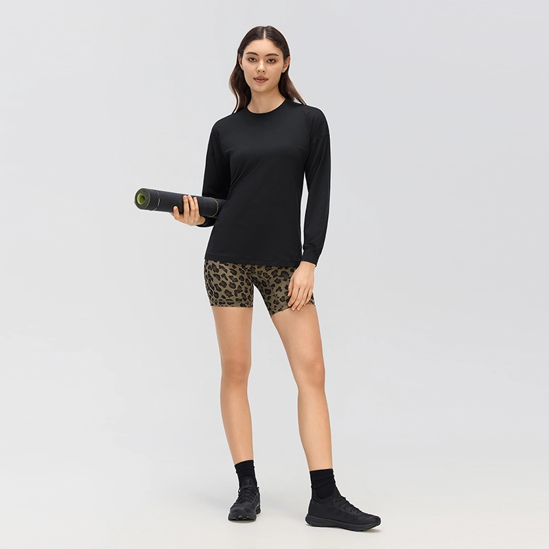 Women's Relaxed Fit Crew Neck Long Sleeve Top with Cuffed Sleeves 3 Full-length studio model wearing a black relaxed-fit crew neck long sleeve top with printed shorts and holding a rolled yoga mat.