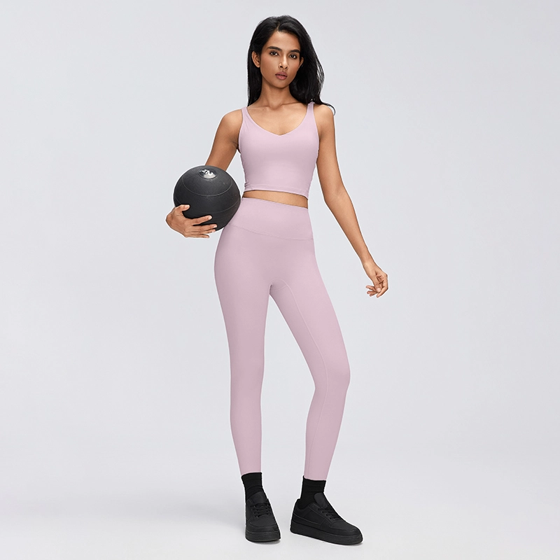 Women's V-Neck Longline Sports Bra with Scoop Back 5 Full-length studio model wearing a Porcelain Pink V-neck longline sports bra with high-waisted leggings while holding a medicine ball.