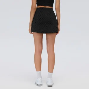 Rear view of a black high-waisted tennis skort showing the flocked polka dot pattern and straight lower hem across the back.